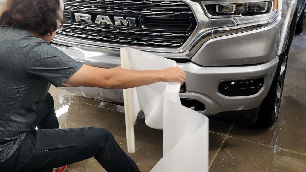 Our installer carefully positions a precision-cut piece of SunTek Ultra PPF across the RAM's front bumper to ensure seamless alignment and complete coverage of high-impact areas.