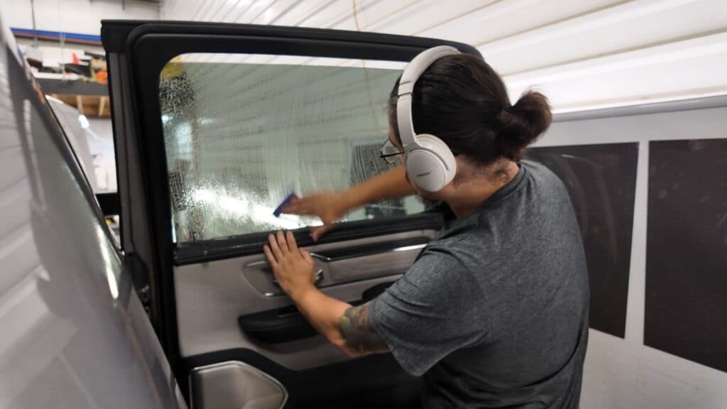 Installer applying SunTek Evolve window film to door glass of a silver Ram 1500 for UV and heat rejection.